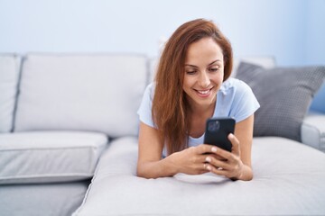 Young woman using smartphone lying on sofa at home