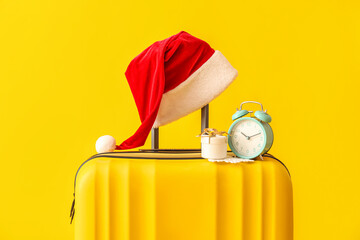 Suitcase with Santa hat, Christmas gift and alarm clock on yellow background