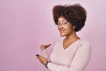 Young african american woman standing over pink background inviting to enter smiling natural with...