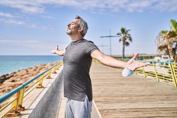 Middle age hispanic man wearing sportswear breathing at seaside - Powered by Adobe