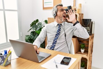 Middle age hispanic business man working at the office wearing operator headset shouting and screaming loud to side with hand on mouth. communication concept. - obrazy, fototapety, plakaty