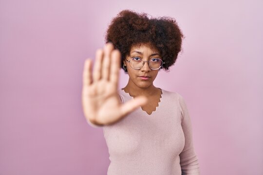 Young african american woman standing over pink background doing stop sing with palm of the hand. warning expression with negative and serious gesture on the face.