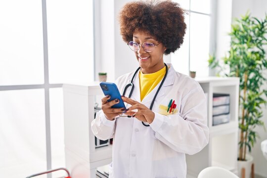 African american woman wearing doctor uniform using smartphone at clinic