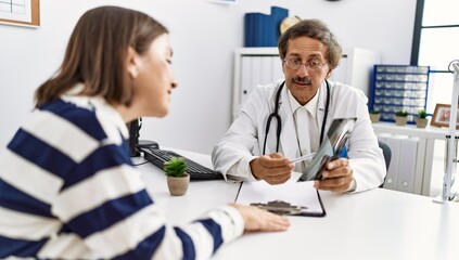 Fototapeta premium Middle age man and woman wearing doctor uniform having medical consultation looking xray at clinic