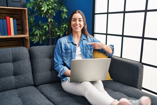 Hispanic woman using laptop at home pointing finger to one self smiling happy and proud