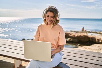 Young hispanic woman smiling confident using laptop and headphones at seaside