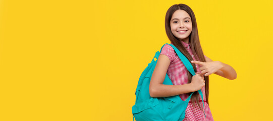 happy school teen girl point finger on backpack on yellow background. Portrait of schoolgirl...