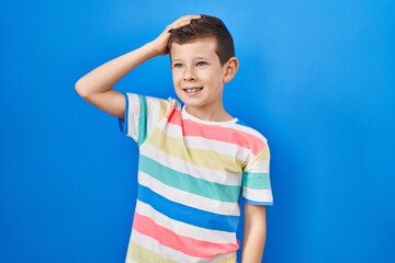 Young caucasian kid standing over blue background smiling confident touching hair with hand up gesture, posing attractive and fashionable