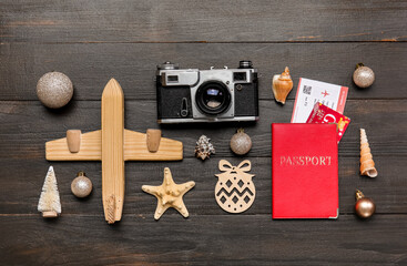 Passport, photo camera, toy airplane, seashells and Christmas decor on dark wooden background