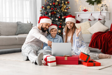 Happy family in Santa hats with laptop at home on Christmas eve