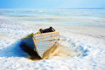 Old blue wooden boat on a seashore surrounded by the snow