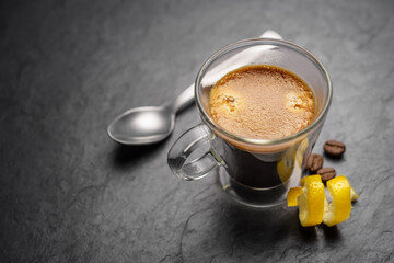Espresso coffee in double wall glass mug with lemon peel.