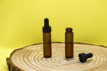 Mockup of brown glass vials with dropper lid on wooden board and on yellow background. Two empty glass bottles and pipette. Concept of body and face care. Selective focus.