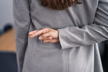 Young beautiful hispanic woman standing with crossed fingers on back at office