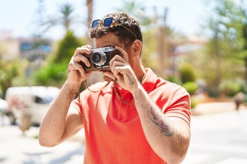 Young hispanic man tourist using vintage camera at street