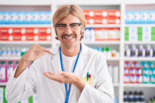 Caucasian man with mustache working at pharmacy drugstore gesturing with hands showing big and large size sign, measure symbol. smiling looking at the camera. measuring concept.