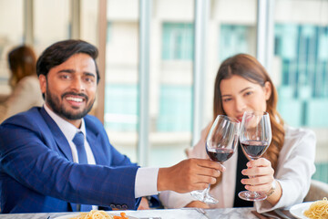 Happy interracial couple with glasses of red wine having date in rooftop restaurant with cityscape view out of window