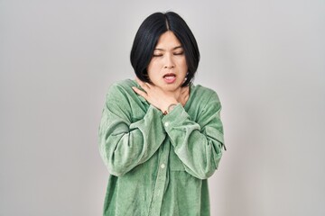 Young asian woman standing over white background shouting suffocate because painful strangle. health problem. asphyxiate and suicide concept.