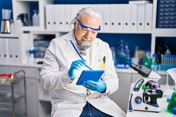 Fototapeta na wymiar Middle age grey-haired man scientist using touchpad at laboratory
