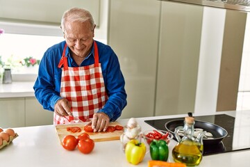 Senior man smiling confident cutting tomato at kitchen