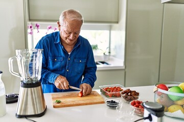 Senior man smiling confident cutting strawberry at kitchen