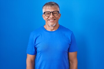 Hispanic man with grey hair standing over blue background with a happy and cool smile on face. lucky person.