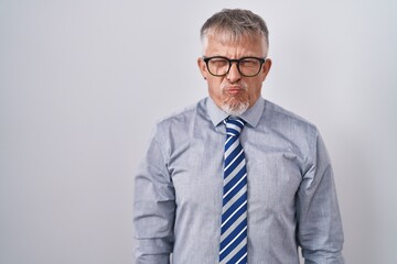 Hispanic business man with grey hair wearing glasses puffing cheeks with funny face. mouth inflated with air, crazy expression.