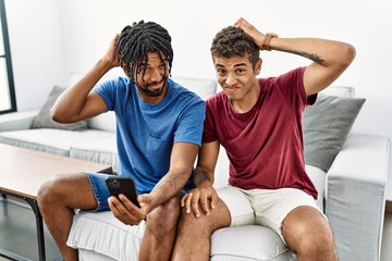Young hispanic men using smartphone sitting on the sofa at home confuse and wondering about...