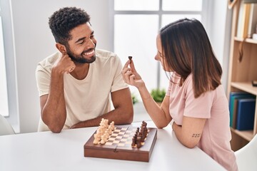Man and woman couple sitting on table playing chess at home