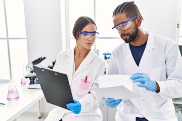 Man and woman scientist partners reading documents at laboratory