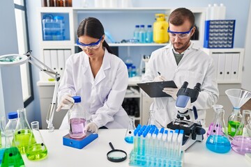 Man and woman scientist partners write on clipboard measuring liquid working at laboratory