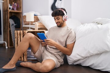 Fototapeta na wymiar Young arab man listening to music sitting on floor at bedroom