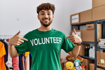 Young arab man pointing with fingers to volunteer uniform at charity center