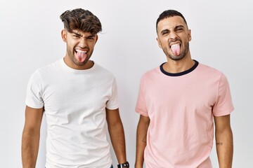 Young gay couple standing over isolated background sticking tongue out happy with funny expression. emotion concept.