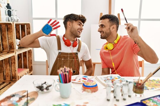 Two hispanic men couple smiling confident showing painted palm hands at art studio