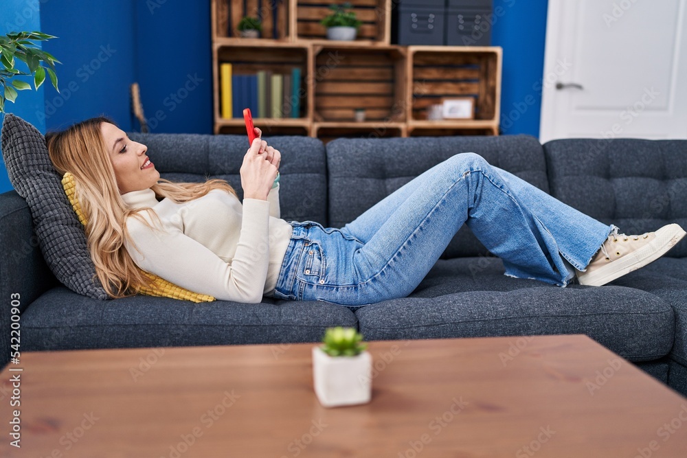 Sticker young blonde woman using smartphone lying on sofa at home