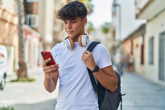 Young hispanic teenager student smiling confident using smartphone at street