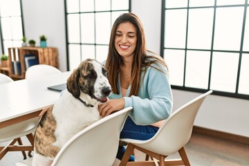 Young woman smiling confident sitting on table with dog at home