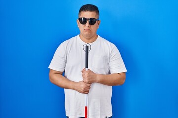 Hispanic young blind man holding cane skeptic and nervous, frowning upset because of problem....