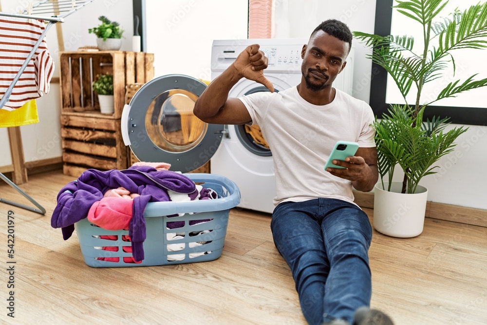 Sticker young african man doing laundry using smartphone with angry face, negative sign showing dislike with