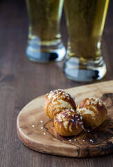 Freshly baked salted pretzel bites with tall glasses of beer in behind.