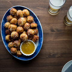 A platter full of salted pretzel bites served with mustard for dipping and beer.