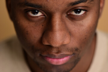Obraz premium Close up shot of a young black man's face with a piercing gaze. Macro studio shot on a beige background.