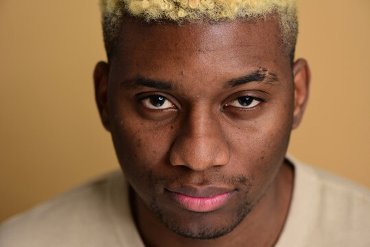 Powerful close up portrait of a young handsome confident black man on a beige background in a studio