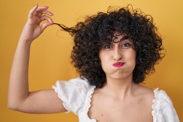Young brunette woman with curly hair holding curl puffing cheeks with funny face. mouth inflated with air, catching air. - obrazy, fototapety, plakaty