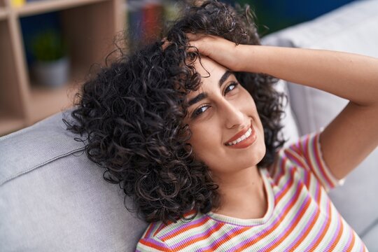 Young middle eastern woman relaxed with hand on head sitting on sofa at home