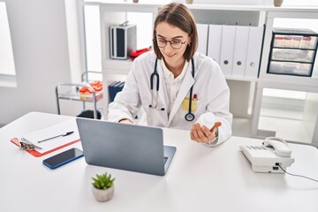 Young caucasian woman doctor using laptop holding pills at clinic