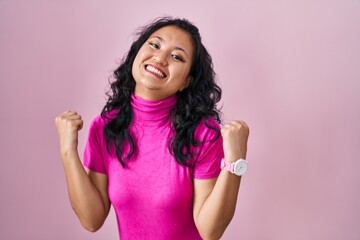Obraz na płótnie Canvas Young asian woman standing over pink background celebrating mad and crazy for success with arms raised and closed eyes screaming excited. winner concept