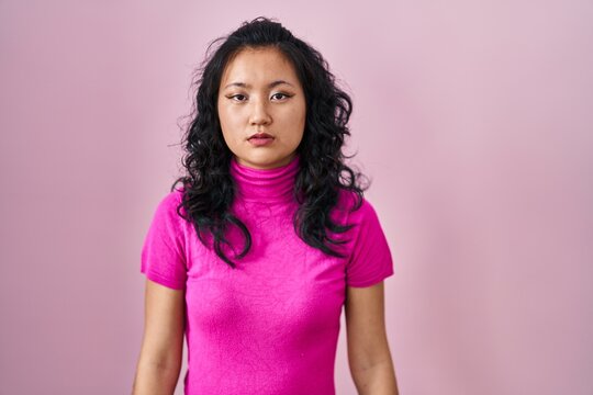 Young asian woman standing over pink background looking sleepy and tired, exhausted for fatigue and hangover, lazy eyes in the morning.