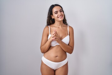 Young hispanic woman wearing white lingerie hands together and fingers crossed smiling relaxed and cheerful. success and optimistic